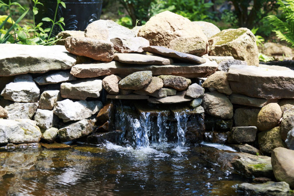 Beautiful backyard garden pond with natural river stones and clear waterfall.